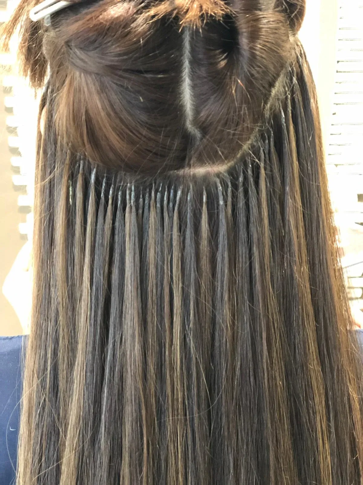 Die Frisur besteht aus langem, glattem, dunklem Haar mit blonden Strähnchen im Nacken.