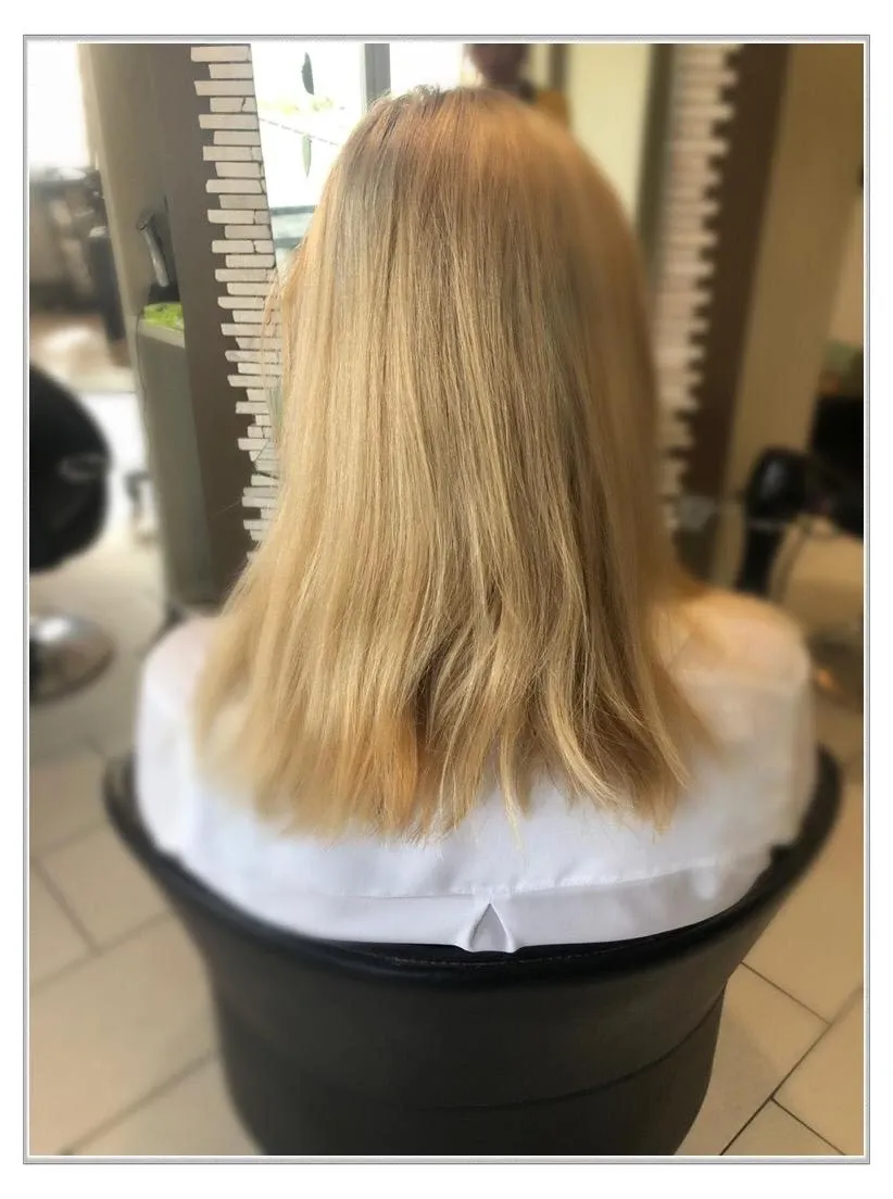 Rückansicht von schulterlangem blondem Haar im Friseurstuhl, mit leicht ungleichmäßigen Spitzen