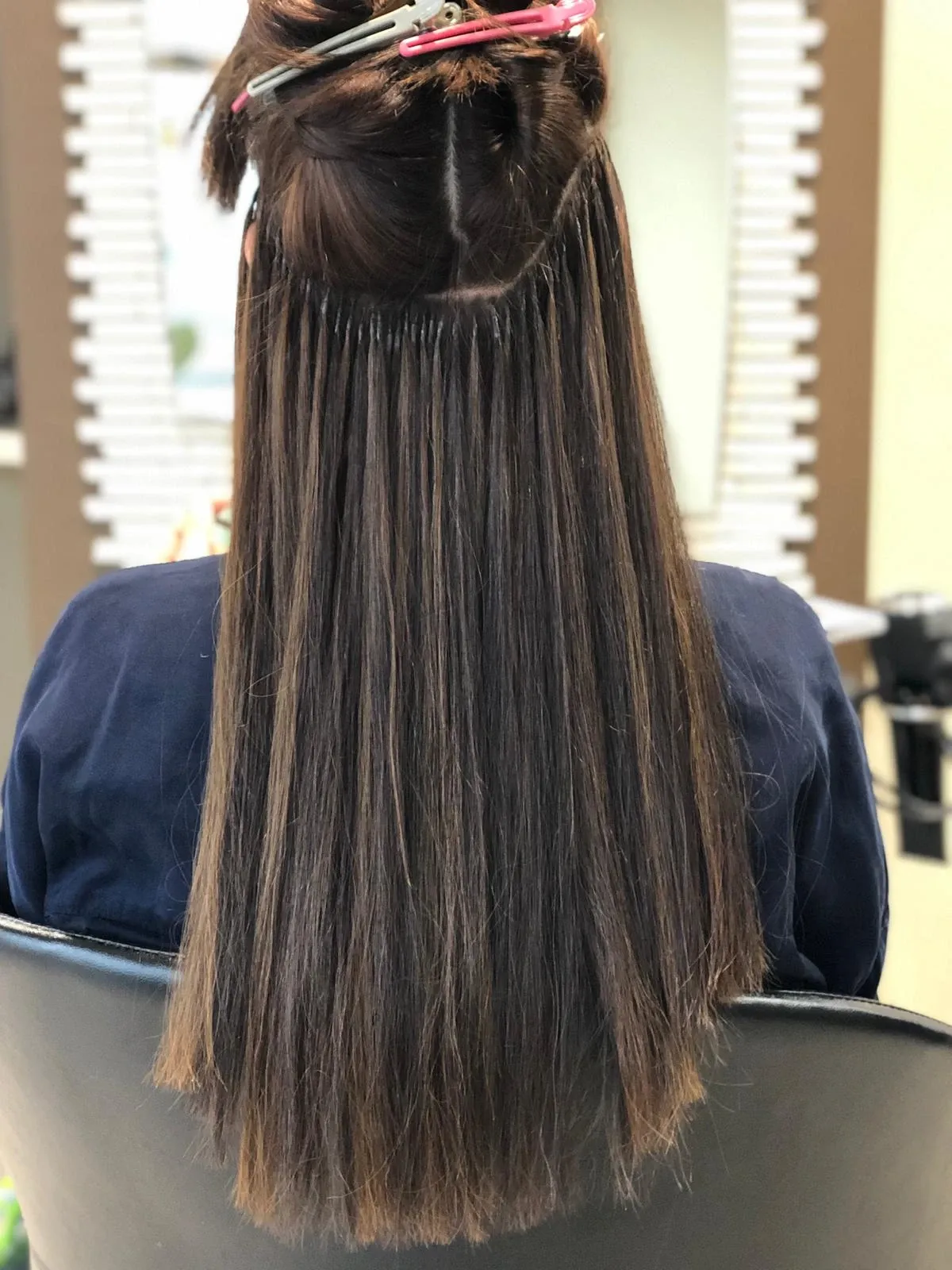 Person mit langen, dunklen Haaren, die teilweise auf einem Friseurstuhl hochgesteckt sind, von hinten gesehen.