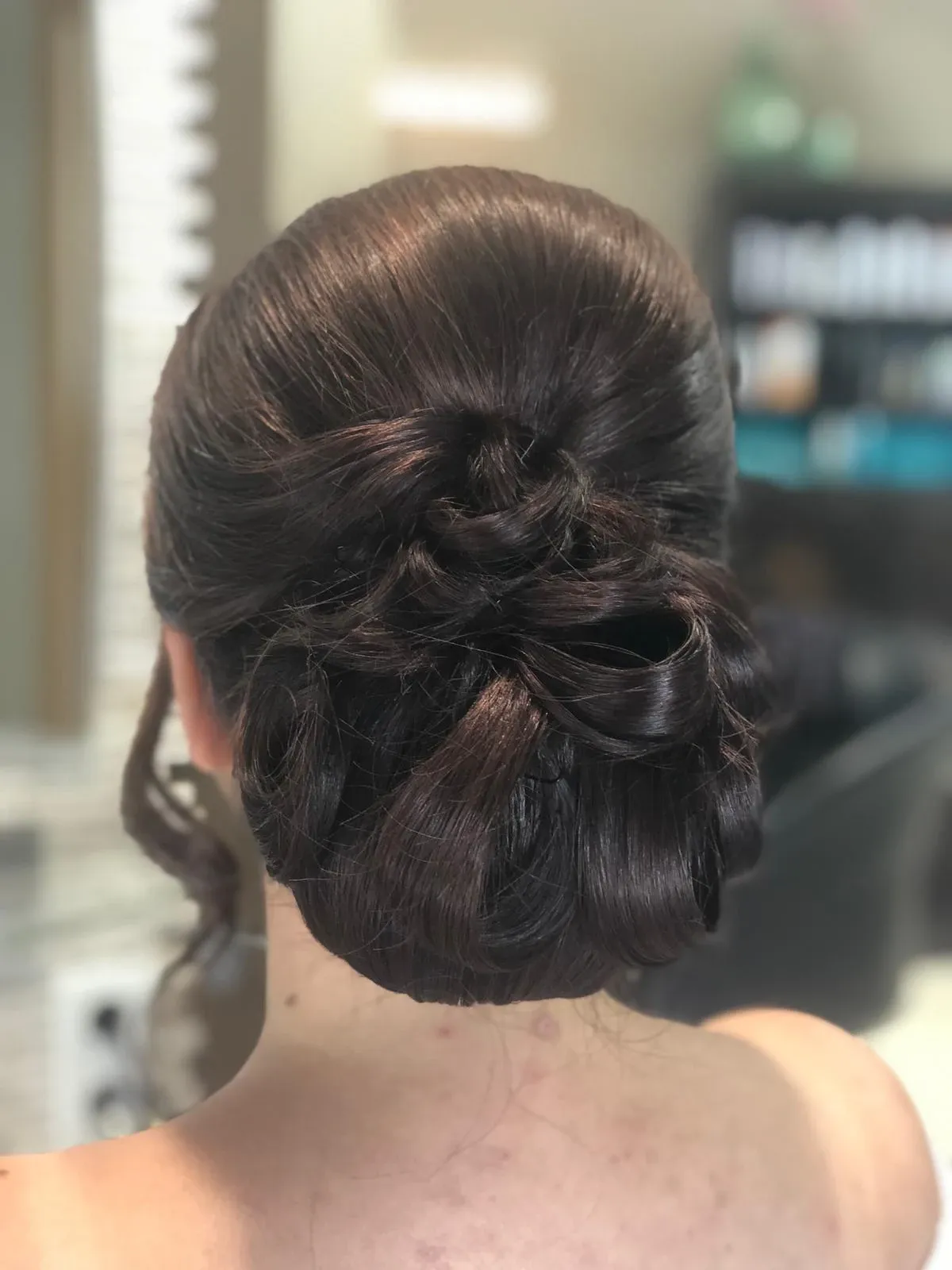 Elegante, dunkle Hochsteckfrisur mit geflochtenem Dutt, von hinten in einem Salon betrachtet