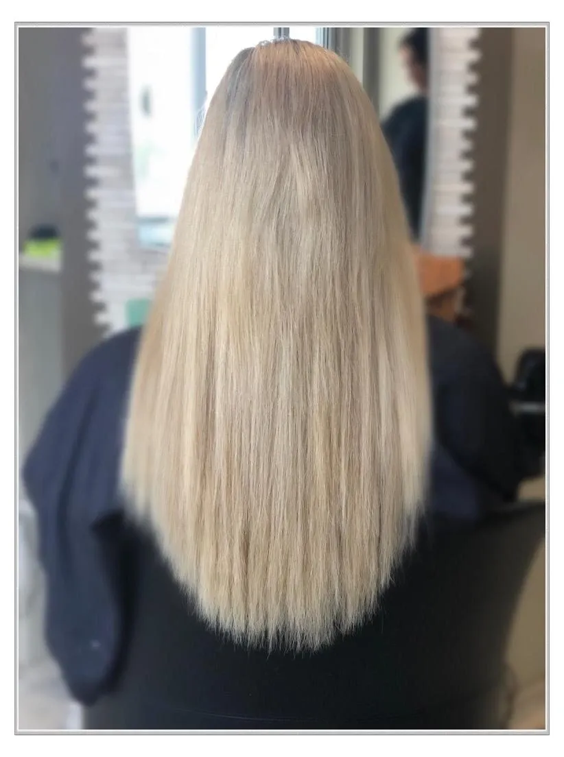 Rückansicht von langem, glattem, platinblondem Haar auf einem Friseurstuhl