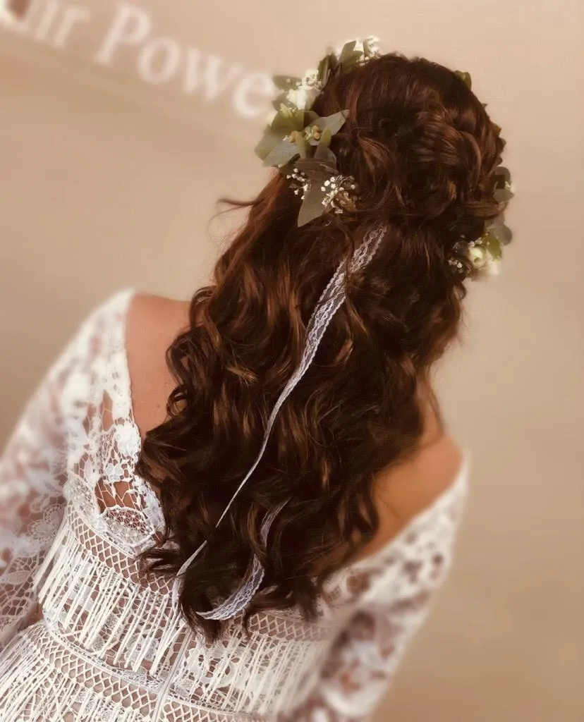 Die Braut, von hinten gesehen, trägt langes geflochtenes Haar, ein weißes Spitzenkleid und einen floralen Haarschmuck.