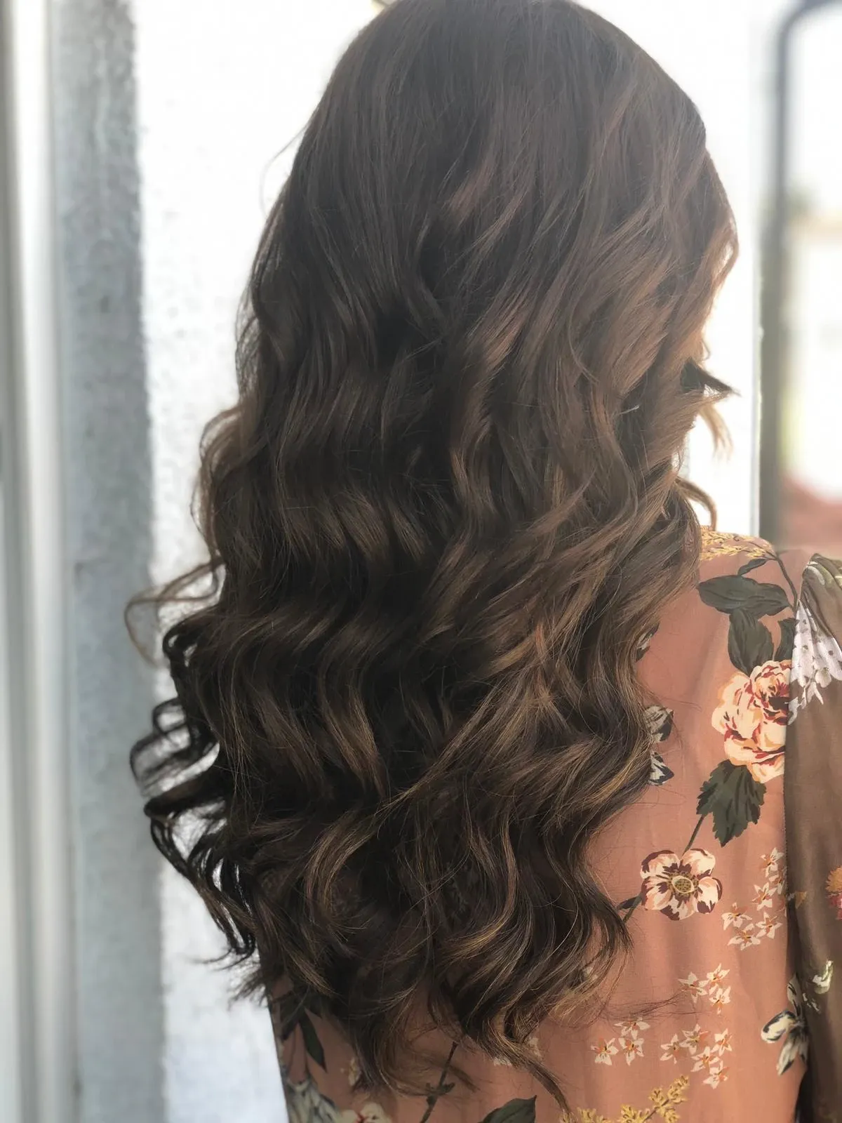 Langes, gewelltes, dunkles Haar mit lockeren Locken über einem Oberteil aus floraler Spitze, von hinten gesehen.