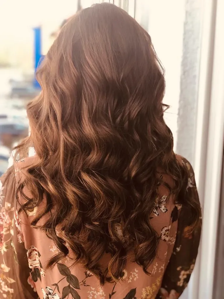 Rückansicht von langem, gewelltem, braunem Haar mit weichen Locken und einem geblümten Kleid in einer hellen Innenraumkulisse