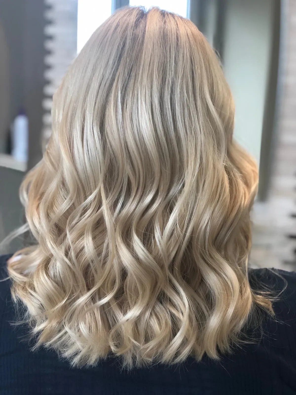 Welliges, blondes, schulterlanges Haar mit dunklerem Ansatz, von hinten im Friseurstuhl gezeigt