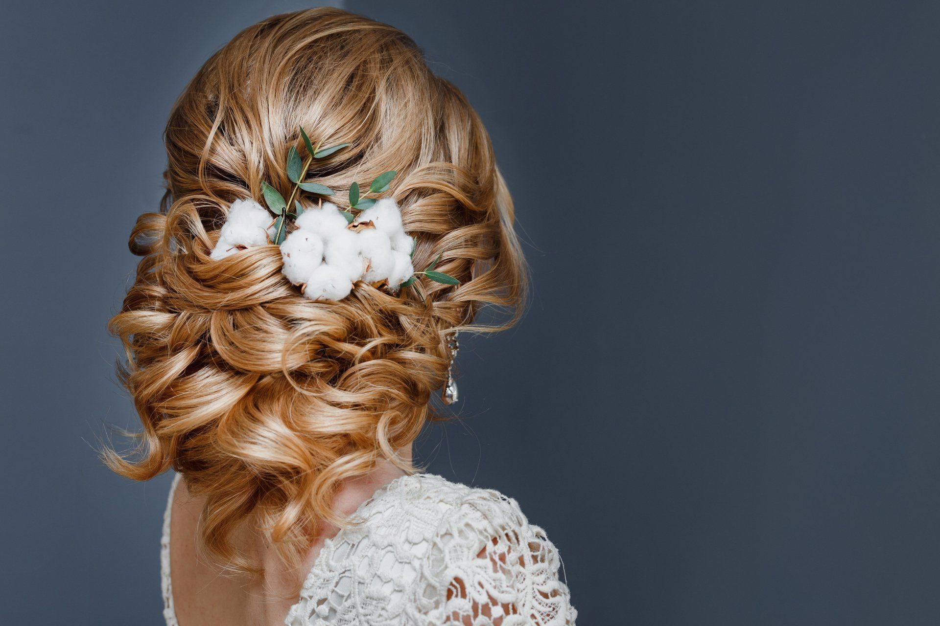 Rückansicht einer eleganten, geflochtenen Hochsteckfrisur mit weißem floralem Haarschmuck auf grauem Hintergrund