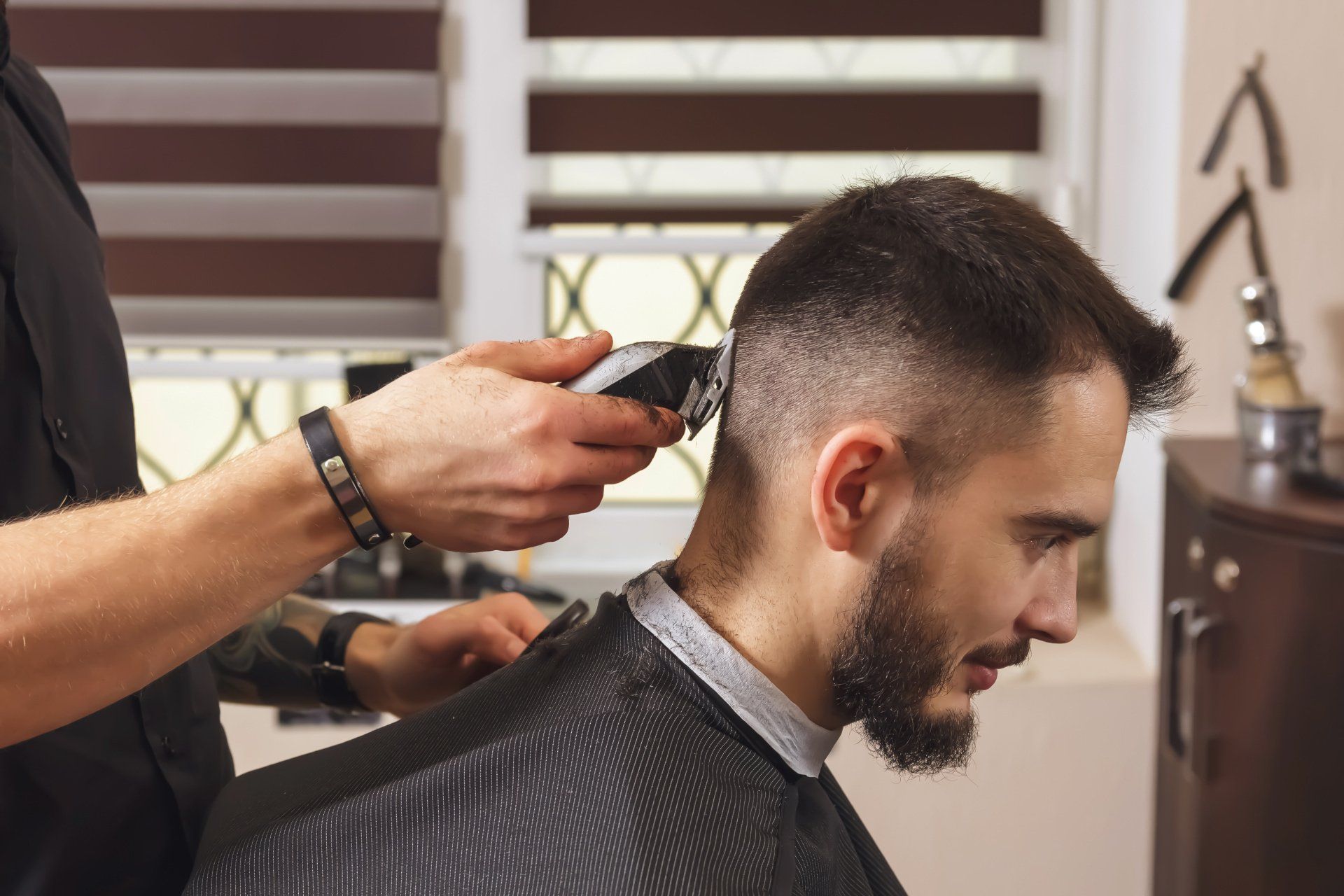 Ein Friseur schneidet einem Mann in einem hellen Salon mit Haarschneidemaschinen die Haare.