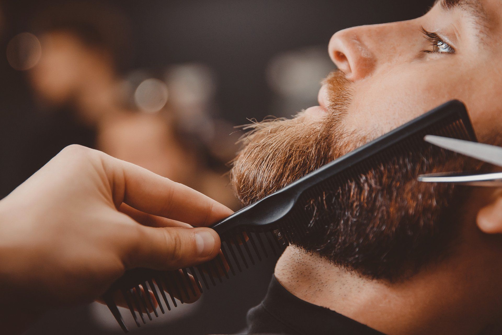 Ein Barbier stutzt einem Mann in einer Nahaufnahme im Salon den Bart mit Schere und Kamm.