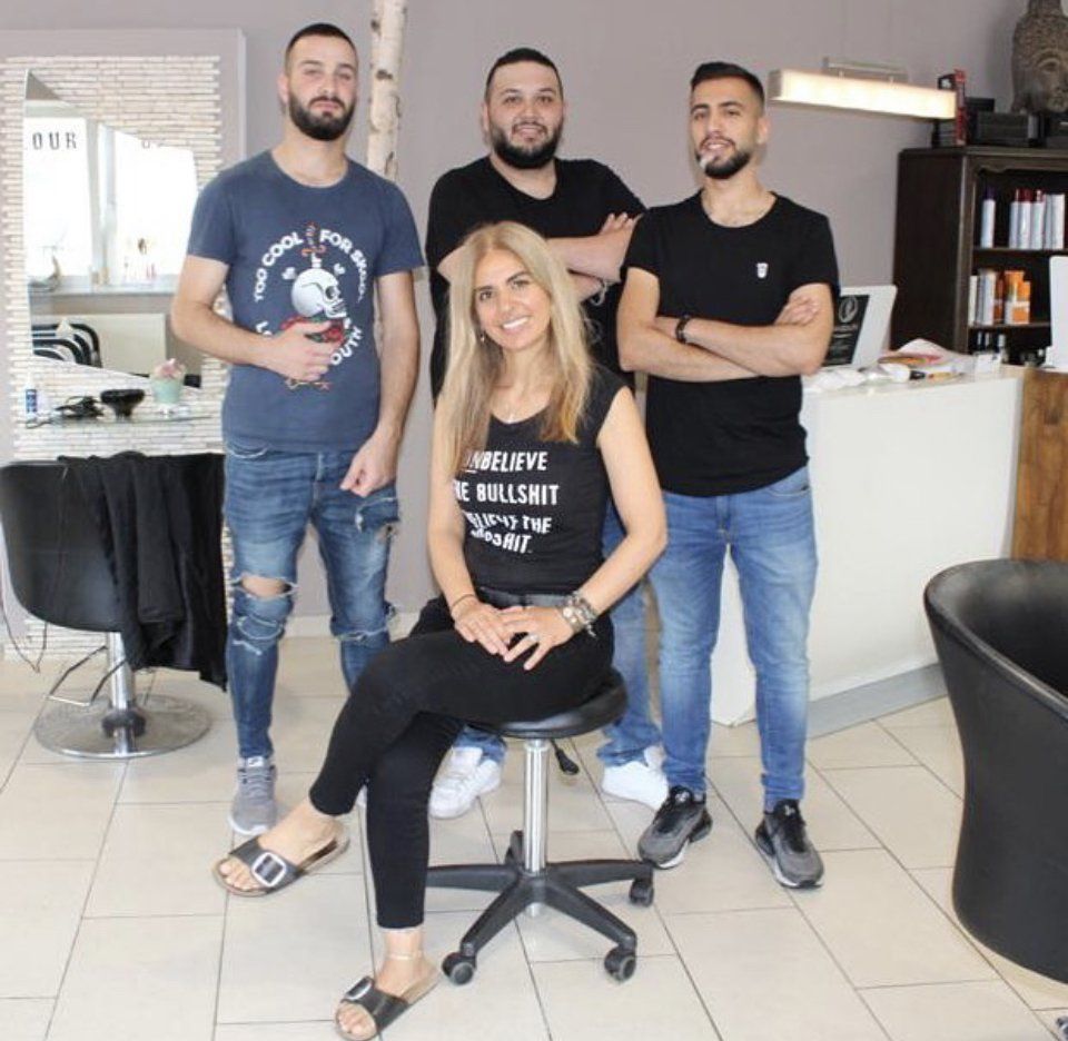 Vier Personen in einem hellen Salon, eine sitzt, drei stehen, die gemeinsam lächelnd posieren.