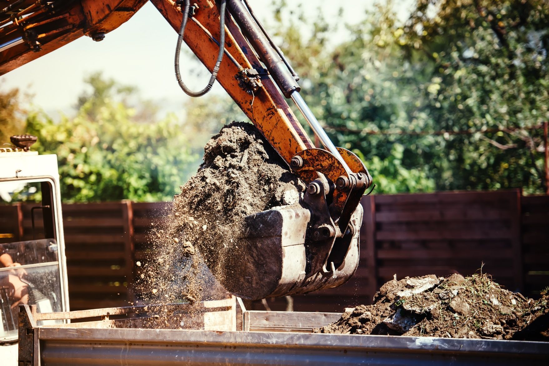 Excavator bucket dumping dirt into a truck bed on a sunny construction site