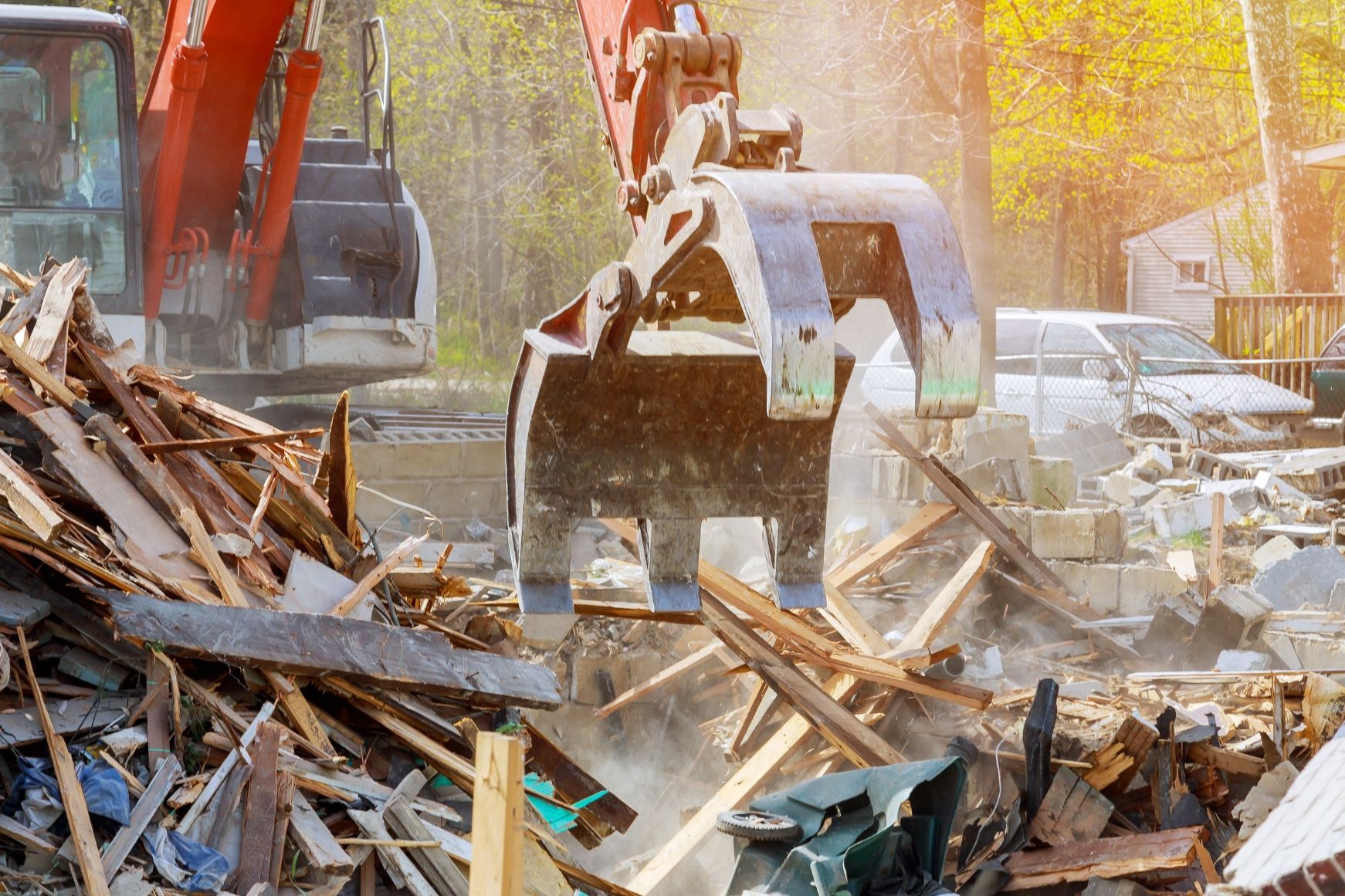 Excavator bucket lifting debris in a construction demolition site with piles of wood and rubble