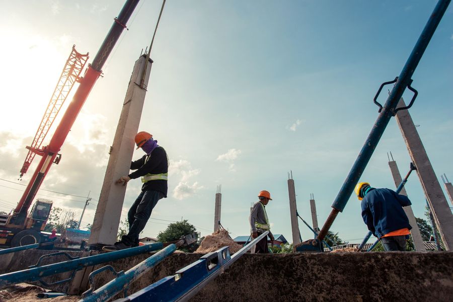 Construction workers in orange helmets working at a building site with cranes and steel beams at sunrise