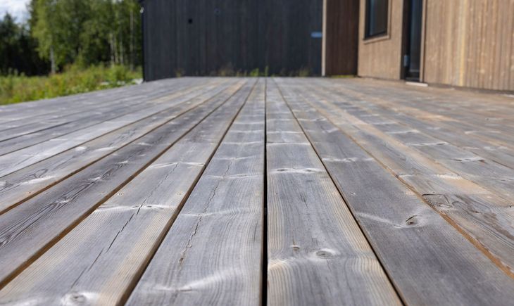Weathered gray wooden deck leading to a dark wooden building with forest in the background
