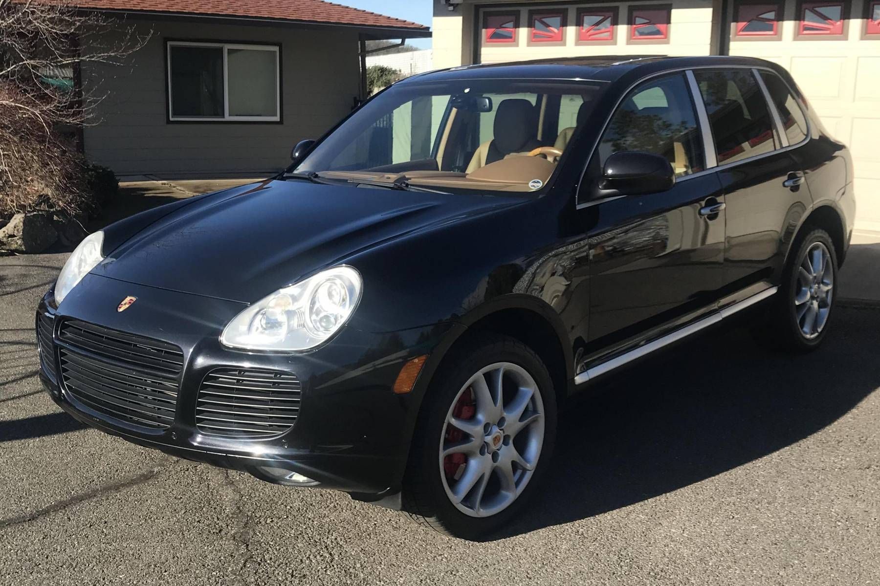 Zwarte Porsche Cayenne SUV geparkeerd voor een gebouw, met bruin interieur en rode remklauwen.