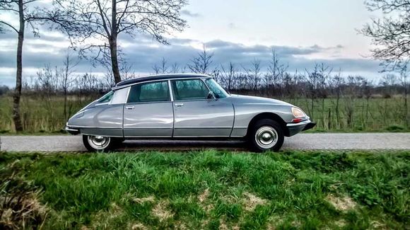 Zilveren vintage Citro&euml;n DS sedan geparkeerd langs de kant van de weg, in een landelijke omgeving met groen gras.