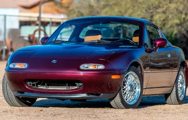 Bordeauxrode Mazda Miata sportwagen met hardtop, chromen wielen, geparkeerd in de buitenlucht.
