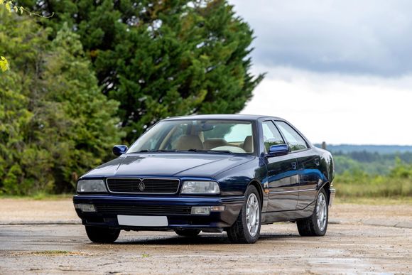Blauwe Maserati-coup&eacute; geparkeerd op een verharde weg met bomen en de lucht op de achtergrond.