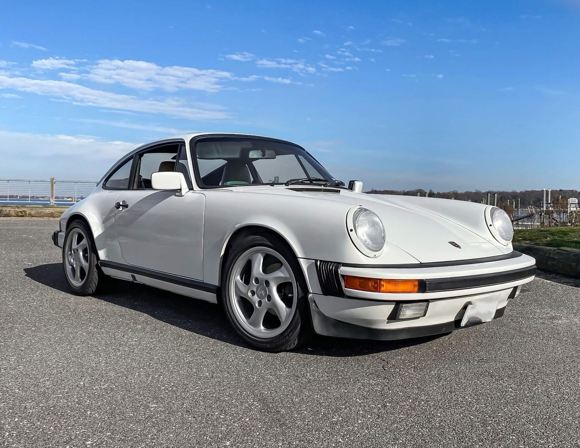 Witte Porsche 911 coupé geparkeerd op asfalt, tegen een blauwe lucht.