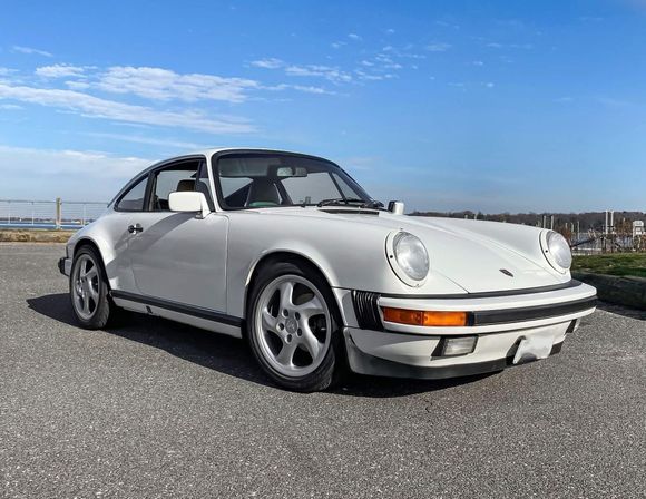 Witte Porsche 911 coup&eacute; geparkeerd op asfalt, tegen een blauwe lucht.