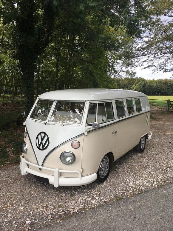 Cr&egrave;me-witte VW-bus geparkeerd op een grindweg, bomen op de achtergrond.