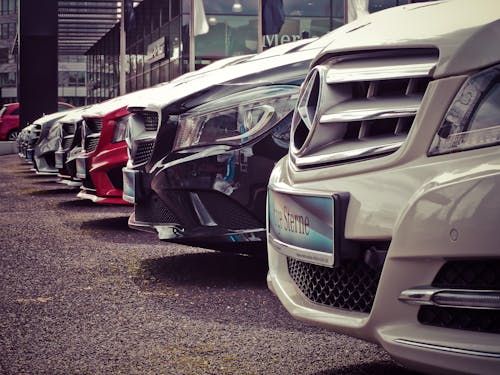 Auto's staan in een rij geparkeerd voor een dealer, waaronder rode, zwarte en witte voertuigen.