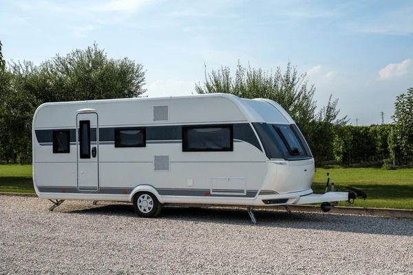 Witte caravan geparkeerd op grind, met bomen en gras op de achtergrond.