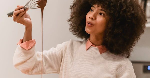 A woman is pouring chocolate into a glass with a whisk.