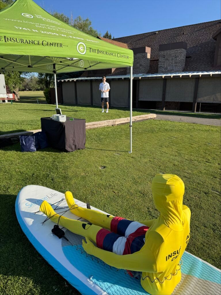 A person in a yellow full-body suit sits on a paddleboard in a grassy field near a tent.