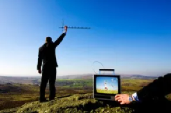 A man in a suit is standing on top of a hill holding an antenna