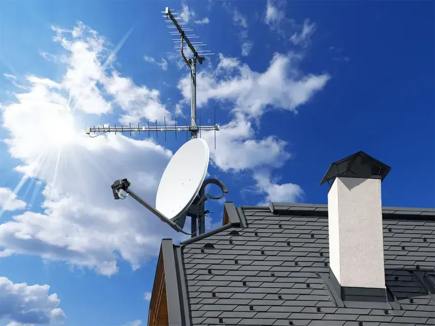 A satellite dish on top of a roof with a chimney