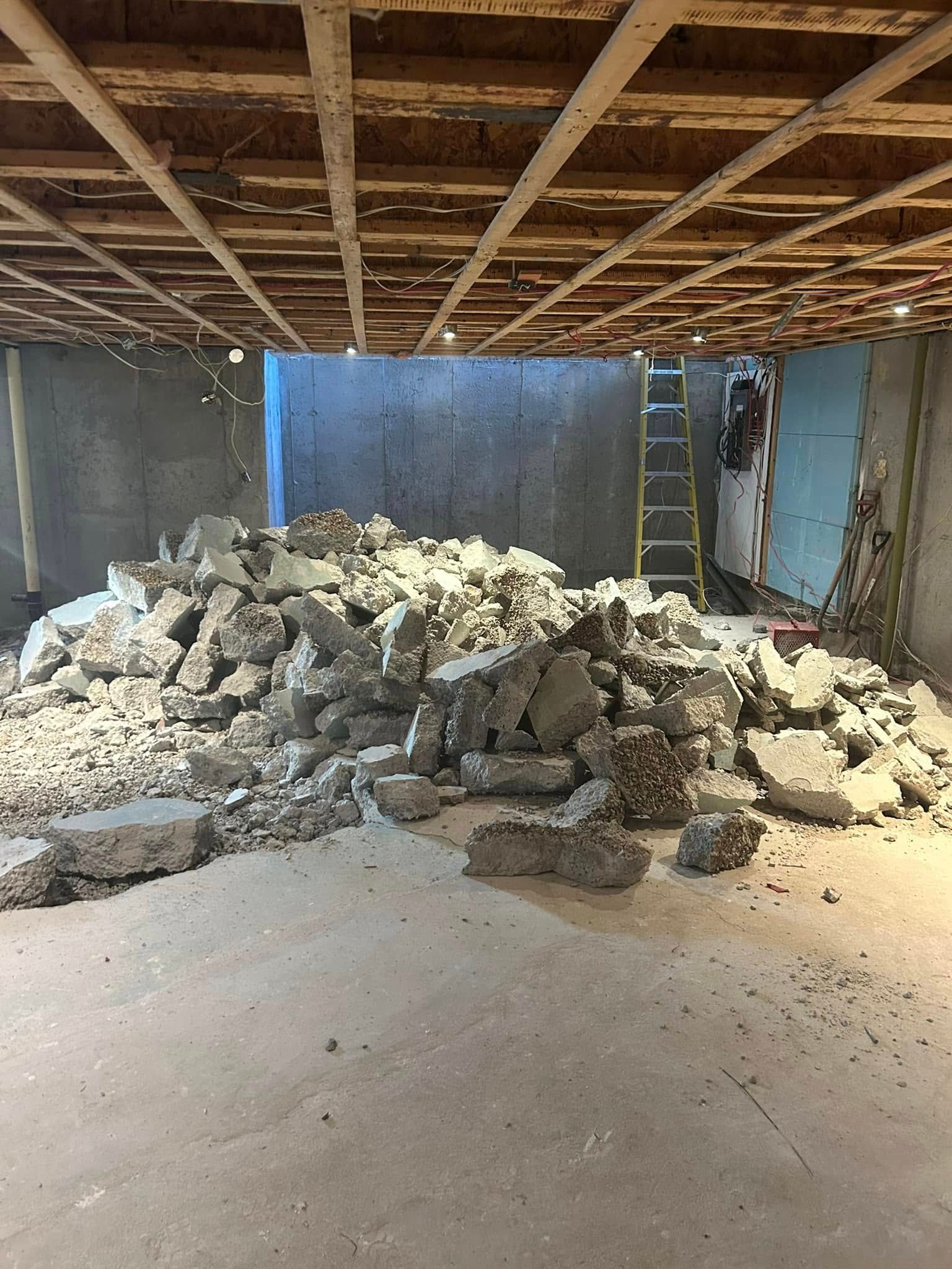 Un tas de béton brisé gît au centre d'un sous-sol inachevé, dont les solives de plafond en bois sont apparentes.