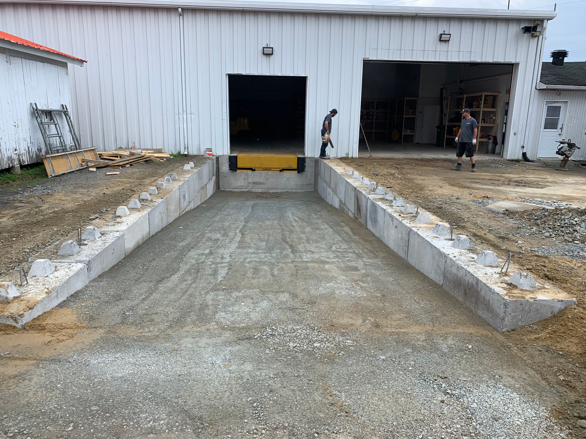 Deux ouvriers se tiennent près d'une rampe de quai de chargement en béton en construction à l'entrée d'un entrepôt.
