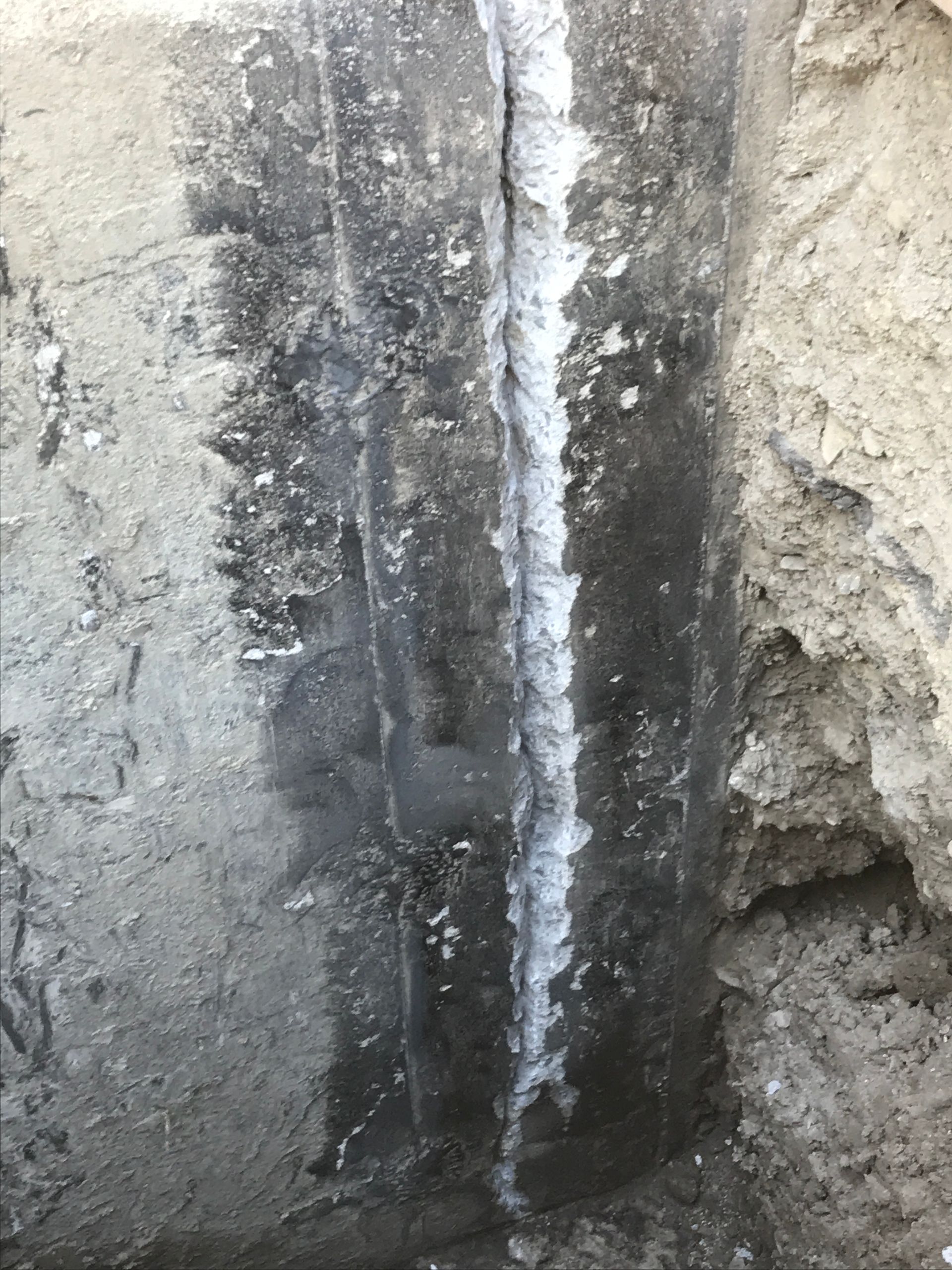 Une fissure verticale dans un mur de fondation en béton gris, avec des dépôts minéraux blancs visibles le long de l'ouverture.