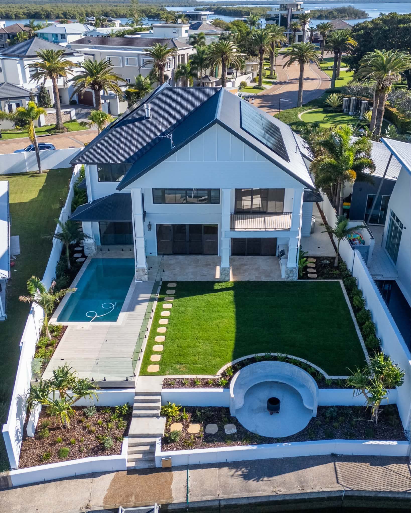 Aerial view of a modern white house with a pool, lawn, and palm trees near the water