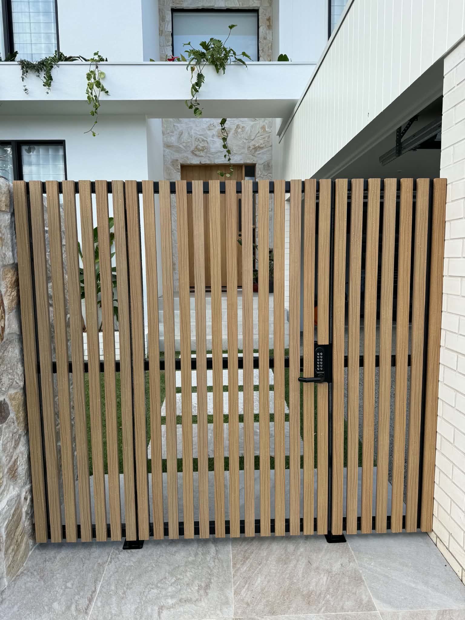 Wooden slatted gate at a modern house entrance, with white walls and a concrete path