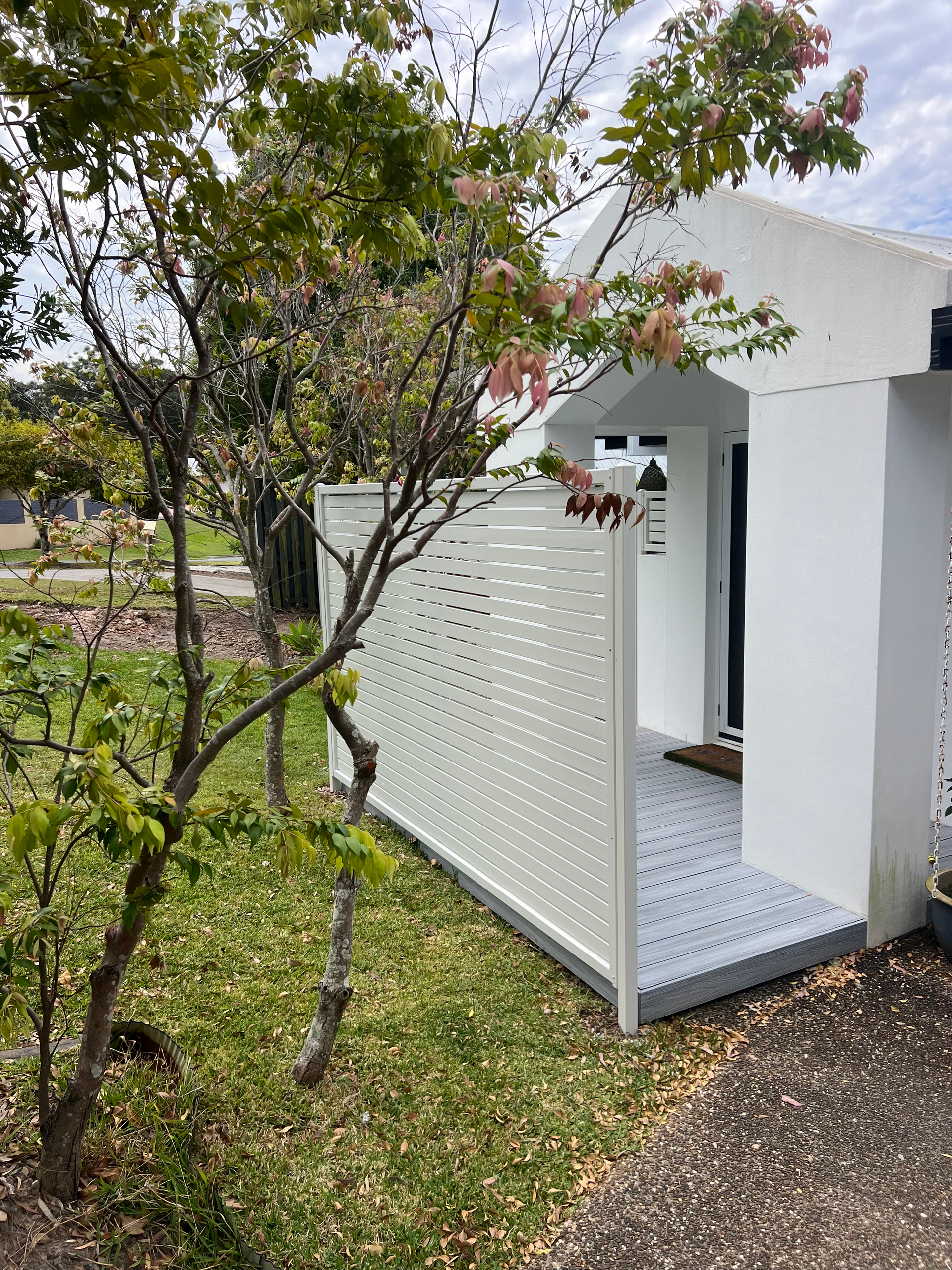 White outdoor entry alcove beside a tree and grassy yard, with lattice wall and tiled floor