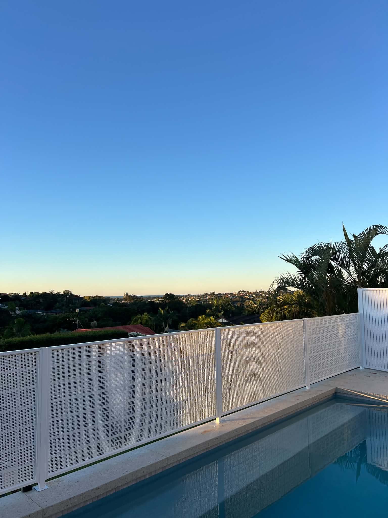 Rooftop pool with white fence, overlooking trees and a clear blue sky at sunset