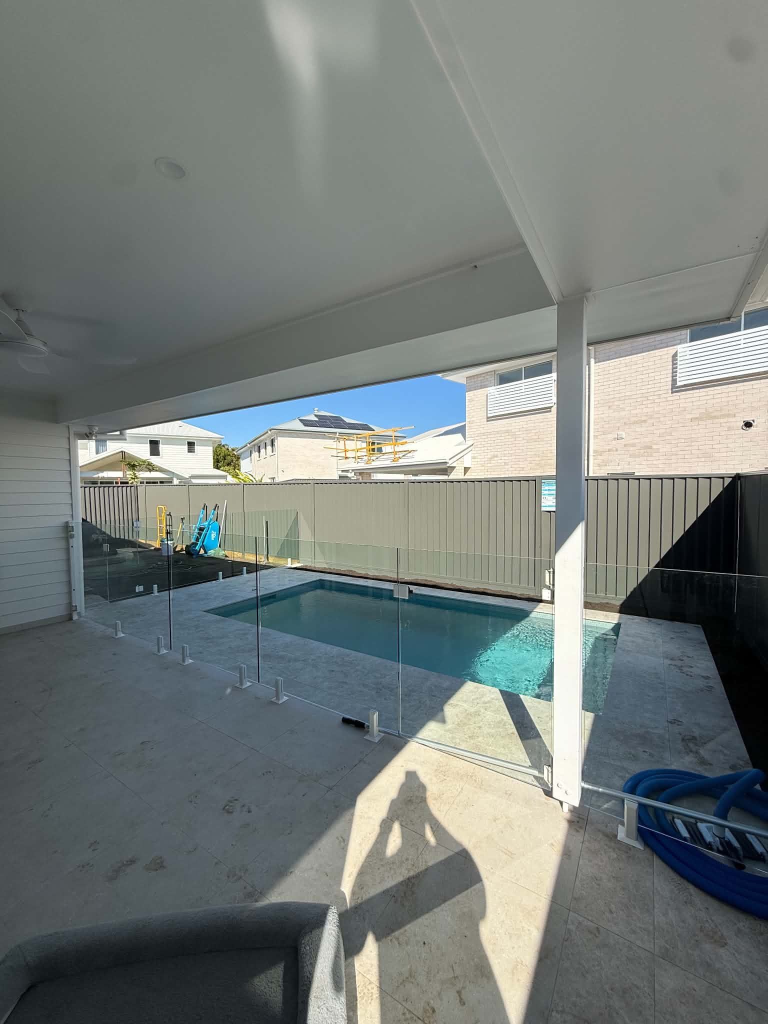 Covered patio overlooking a backyard pool with beige fence and bright sunlight