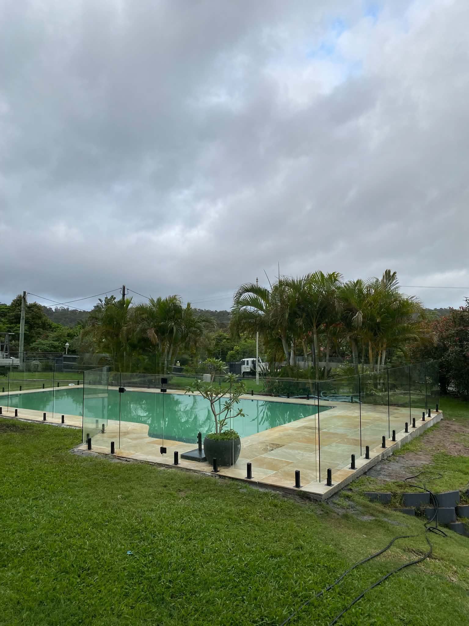 Outdoor swimming pool with turquoise water, surrounded by grass and trees under a cloudy sky