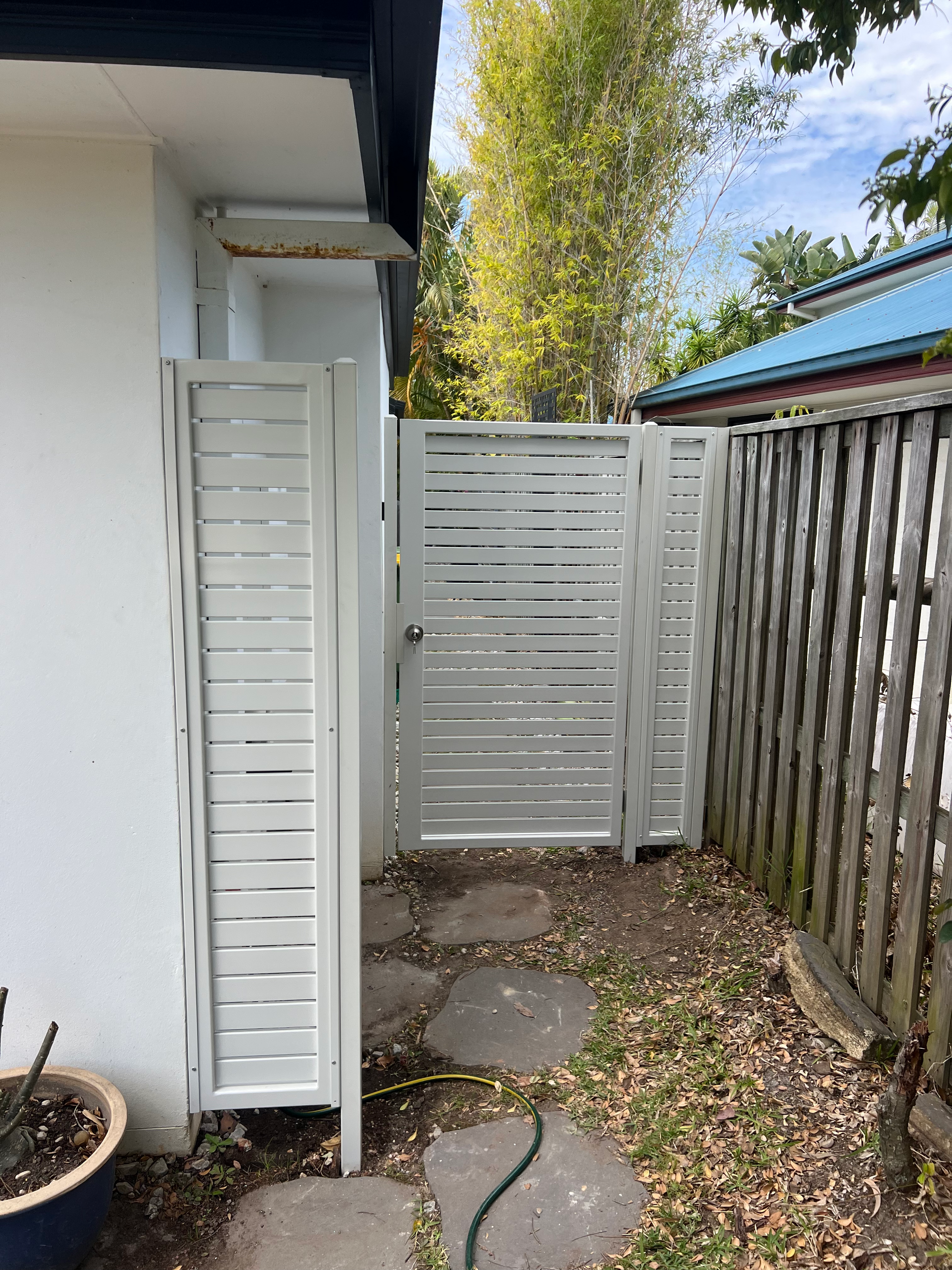 Narrow side yard with white gate, gravel path, stepping stones, and wooden fence beside a house.