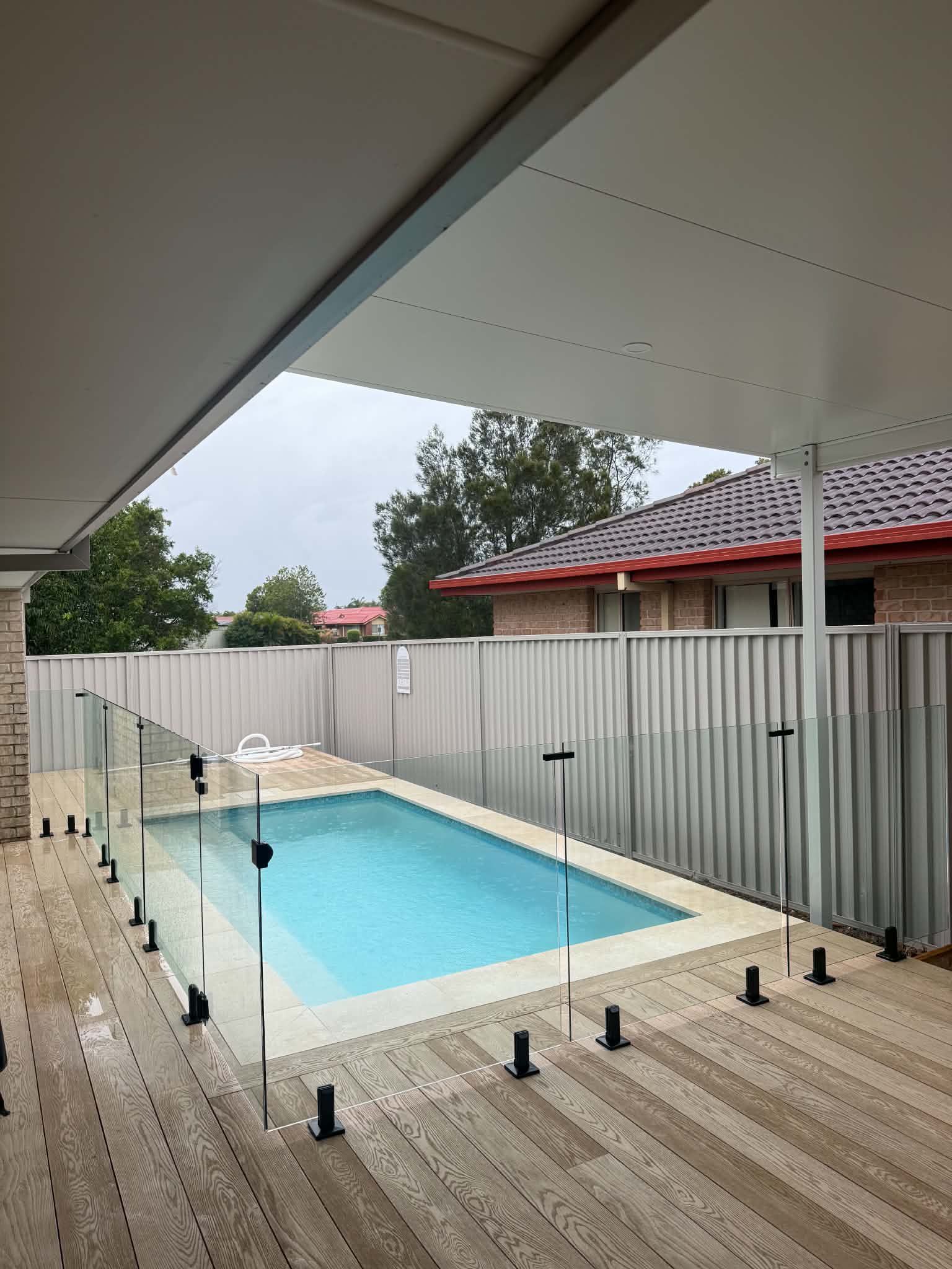Covered patio overlooking a small backyard pool with turquoise water and white privacy fencing