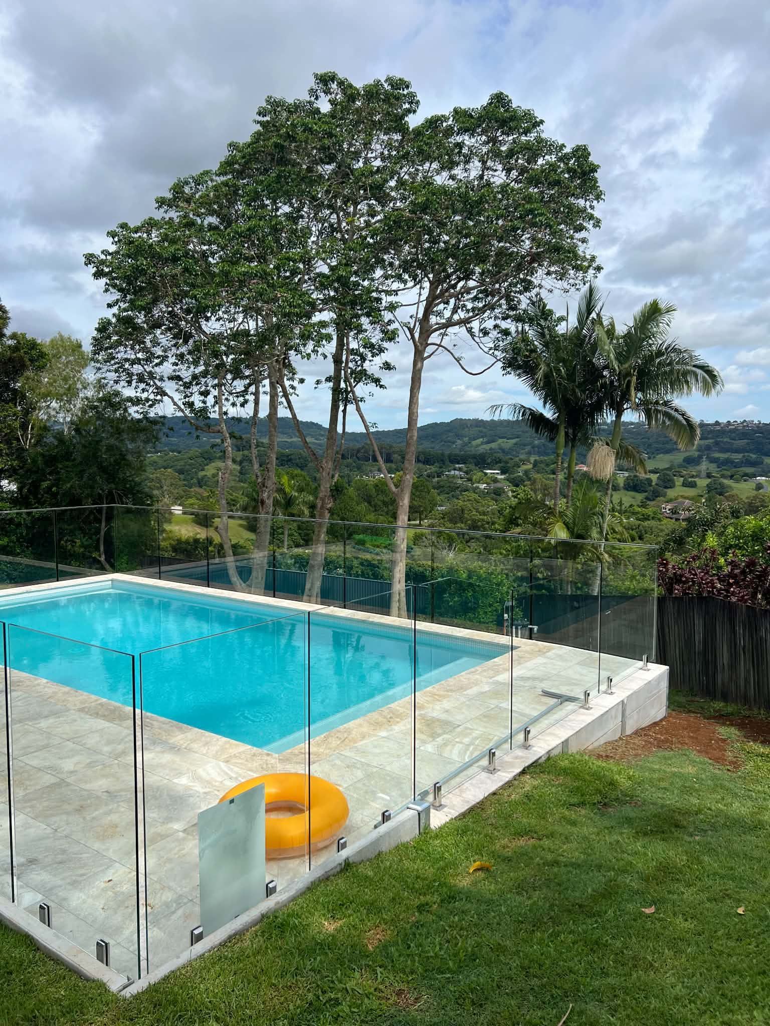 Rooftop pool with glass railing, turquoise water, yellow float, and trees overlooking a scenic valley.