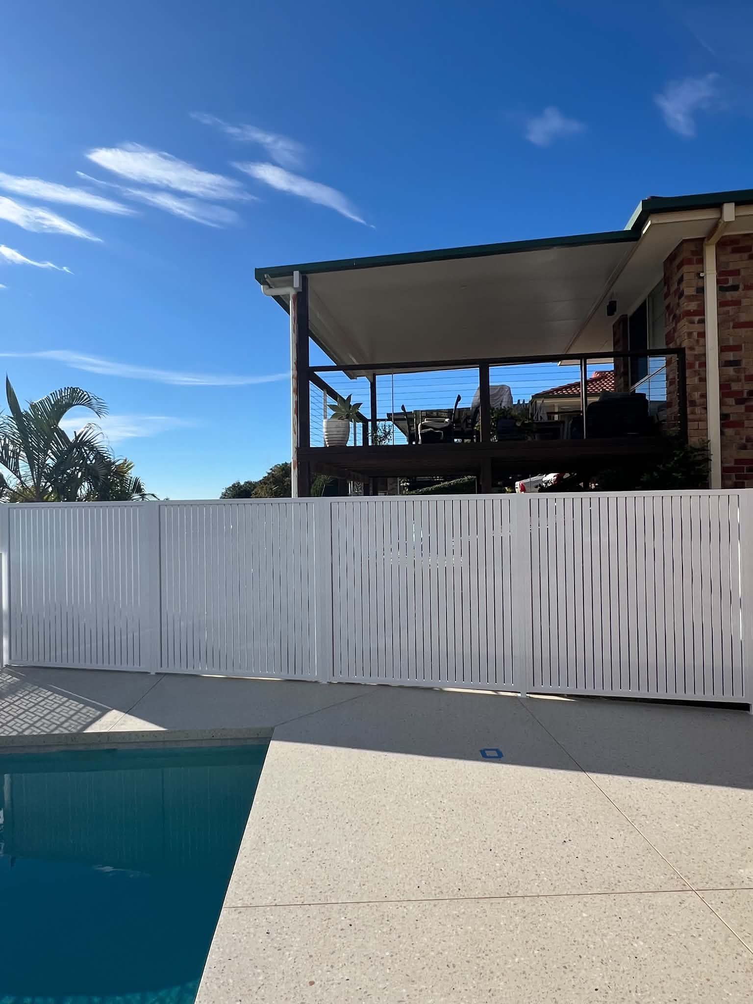 Backyard pool beside a white fence and covered patio under a blue sky