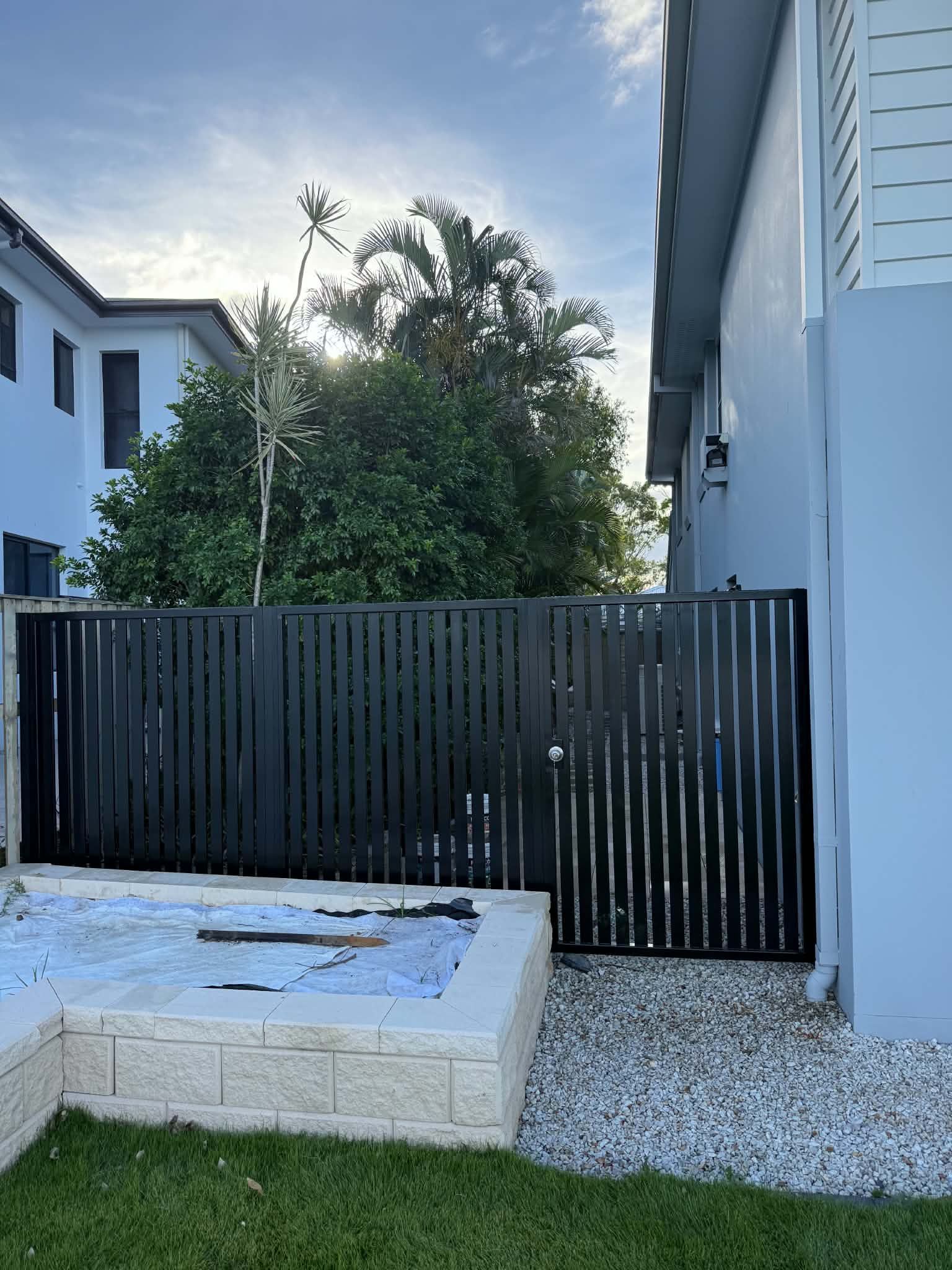 Backyard patio with black wooden fence, white gravel, and modern house walls on both sides