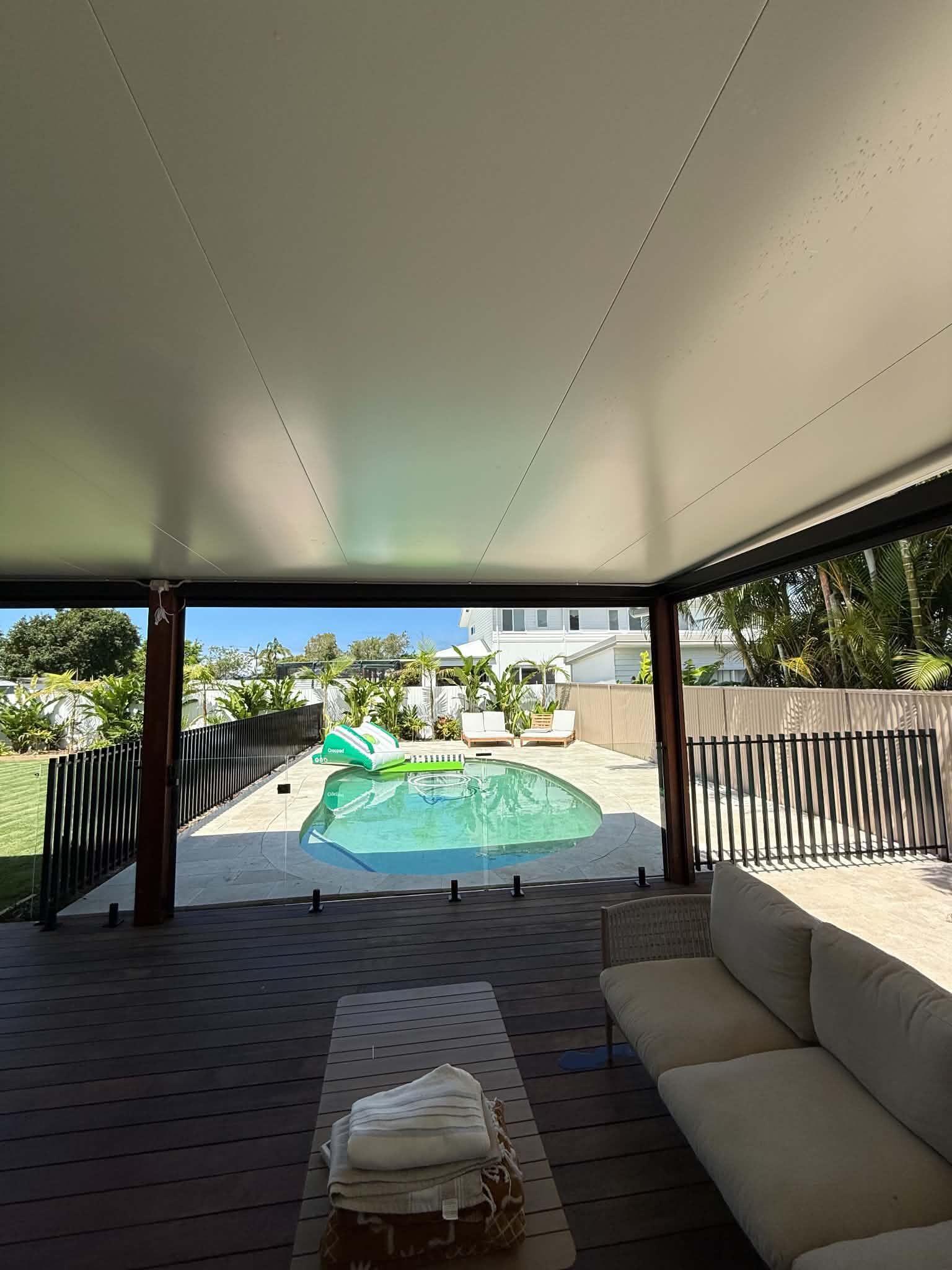 Covered patio overlooking a backyard pool with a green umbrella and outdoor seating