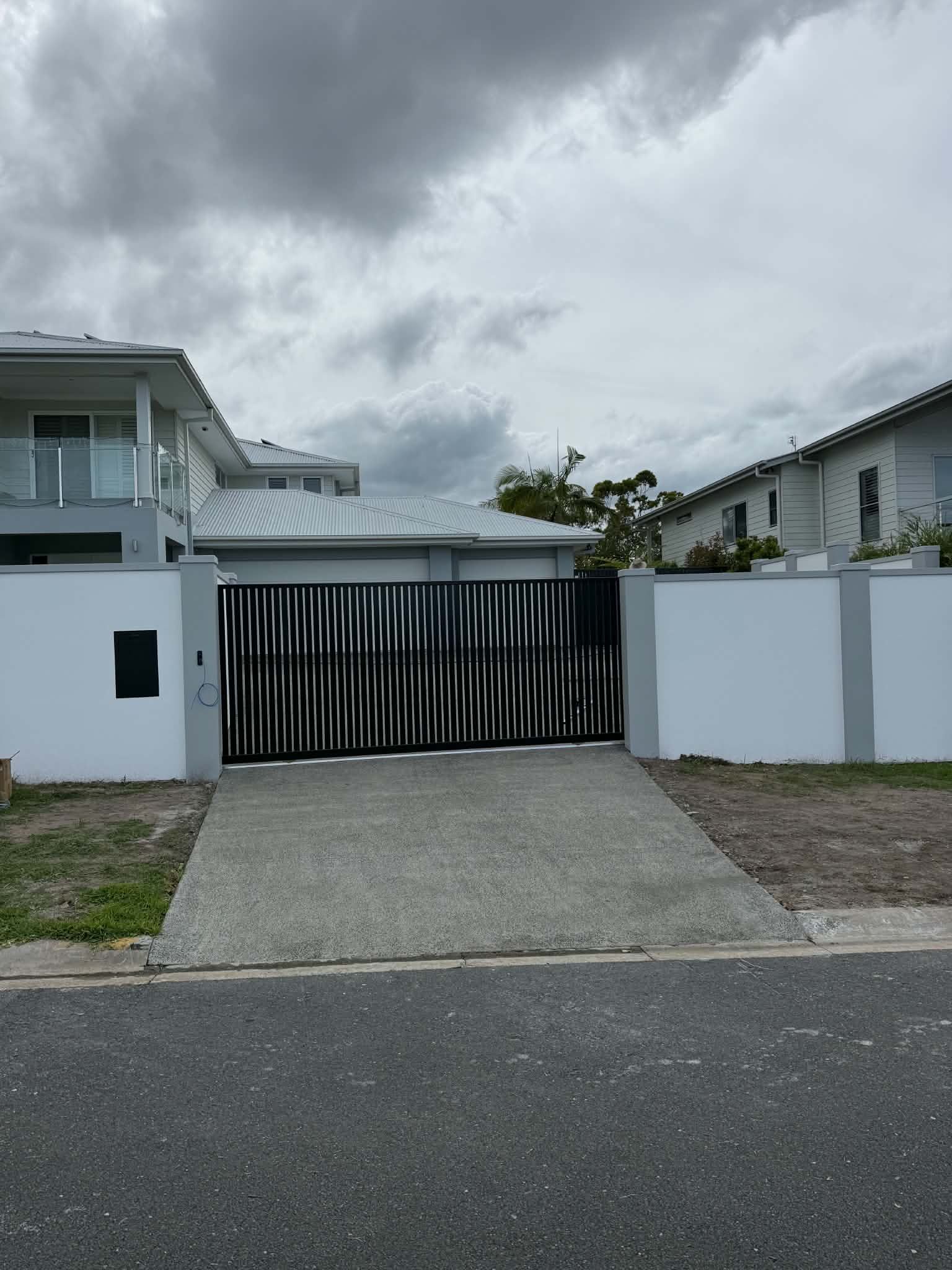 Modern house driveway with black gate, white walls, and cloudy sky