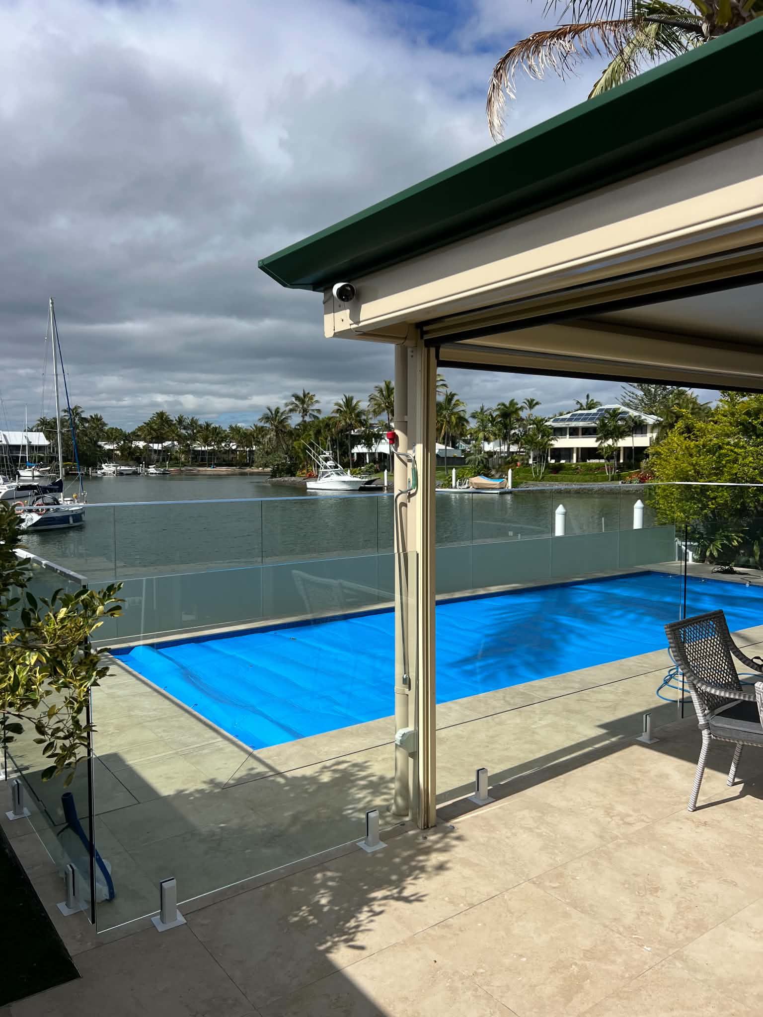 Outdoor patio overlooking a swimming pool with blue cover, tennis court, and a covered seating area