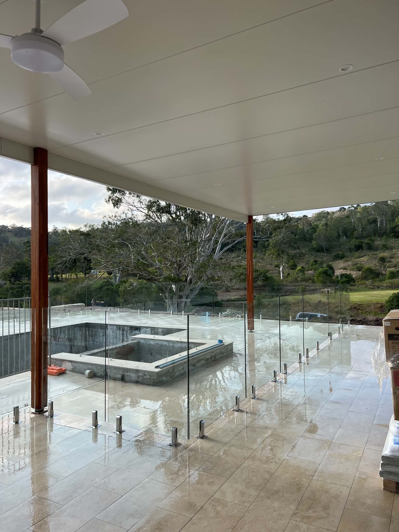Covered patio overlooking a wet pool deck and lake after rain, with lounge chairs and trees beyond