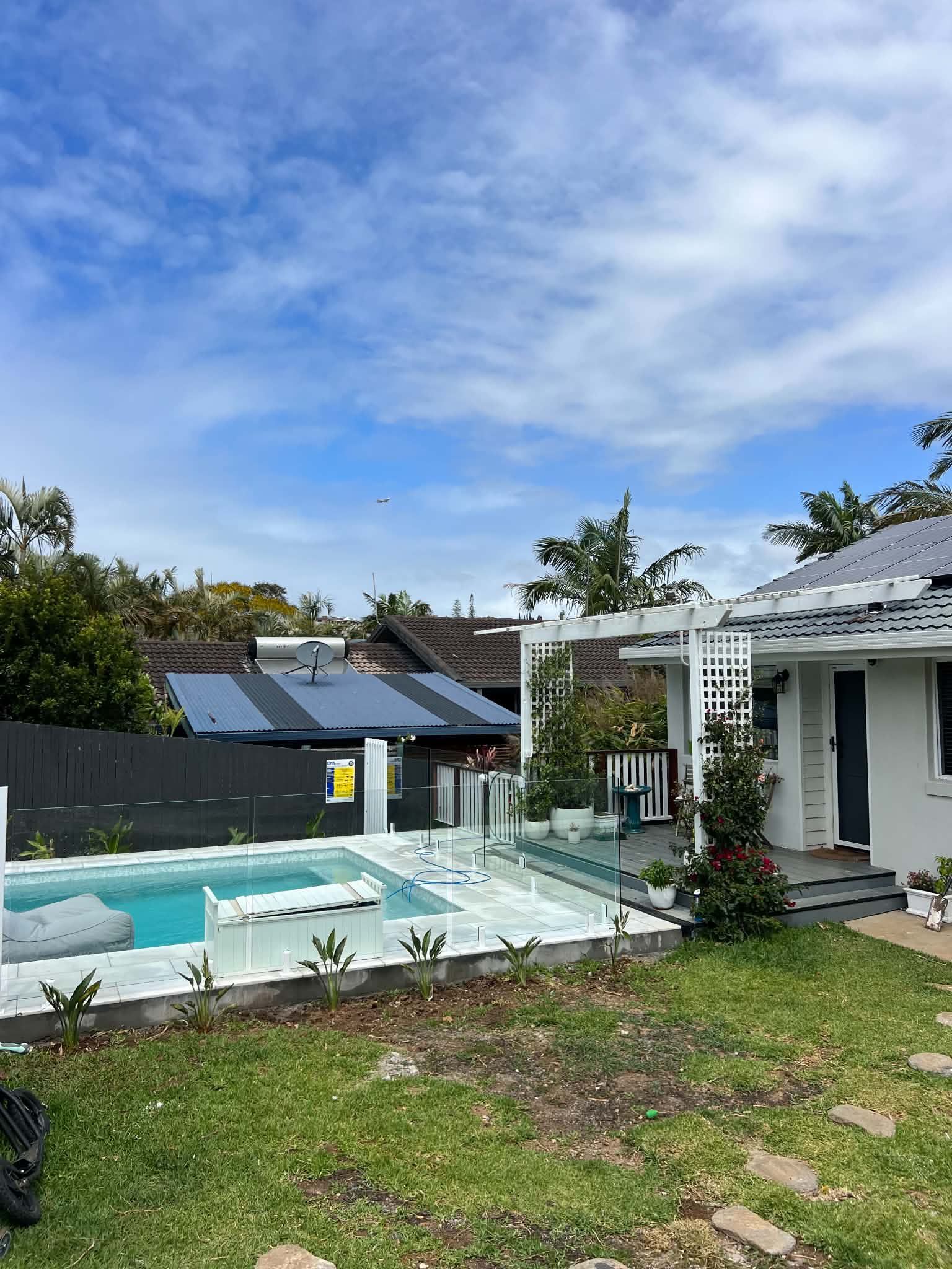 Modern backyard with a swimming pool, white patio pergola, and grassy lawn under a blue sky