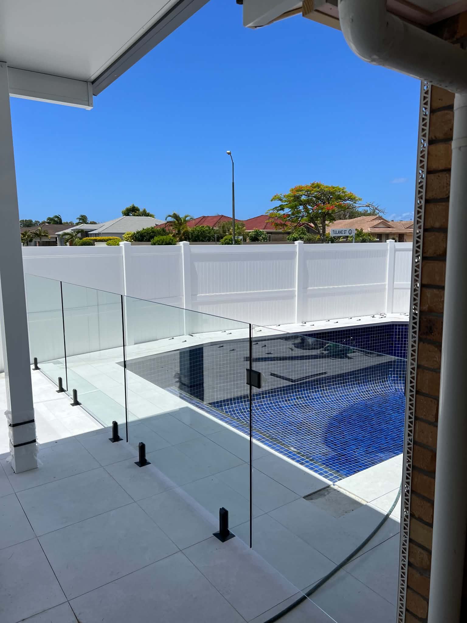 Modern patio overlooking a blue-tiled pool, white fence, and clear blue sky